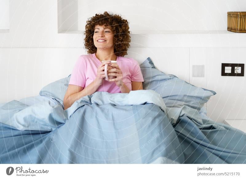 Lächelnde Frau mit einer Tasse Heißgetränk auf dem Bett genießen aufwachen trinken Kaffee räkeln Morgen Schlafzimmer Wochenende LAZY sich[Akk] entspannen
