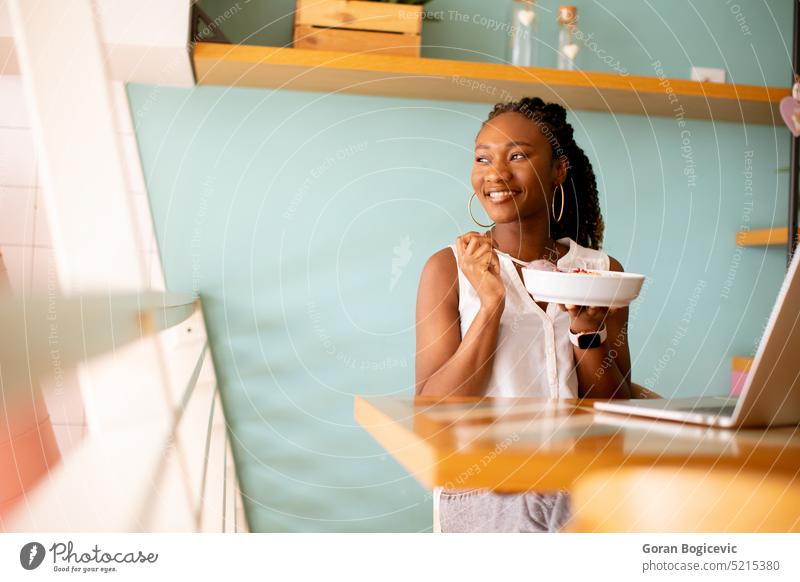 Junge schwarze Frau, die ein gesundes Frühstück zu sich nimmt, während sie in einem Café am Laptop arbeitet Internet Computer modern Freiberufler Glück
