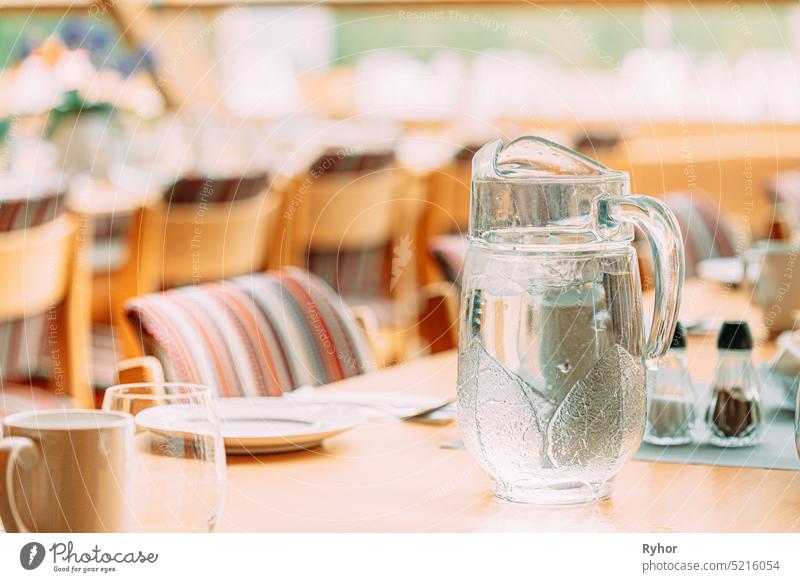 Gemütliches Interieur eines Sommercafés. Krug mit eiskaltem Eiswasser auf dem Tisch und ausgelegtem Besteck Dekoration & Verzierung eisig hell Ansicht