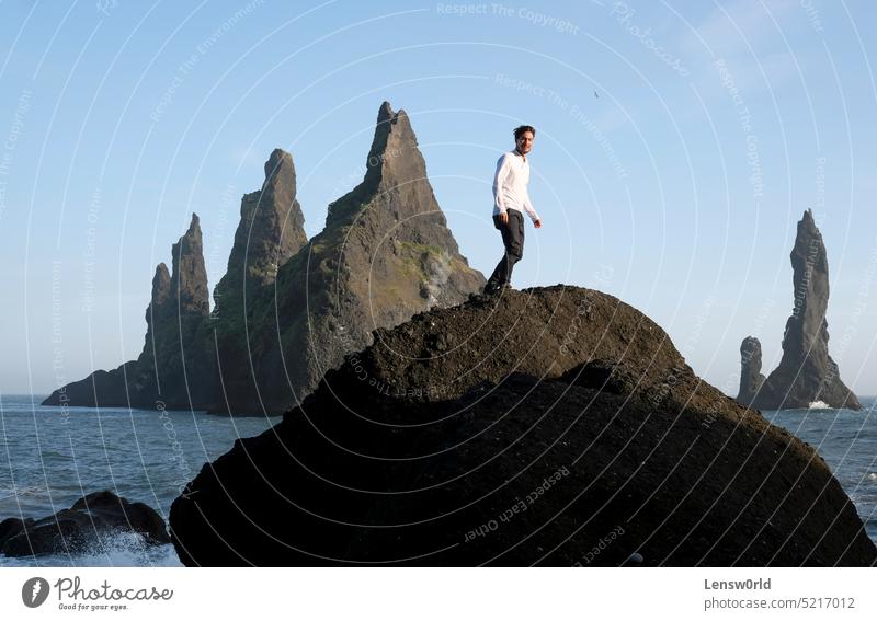 Mann steht auf einem Felsen am Reynisfjara Black Beach, Island, mit Wind in den Haaren Abenteuer schwarzer Strand blau Klippe Konzept Freiheit gutaussehend