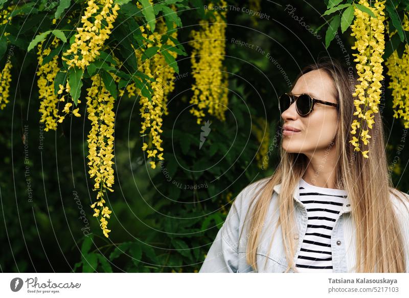 Eine Frau bewundert die blühenden Büschel von Laburnum anagyroides bei einem Frühlingsspaziergang im Park Sommer Menschen Person Blumen Erwachsener Blütezeit