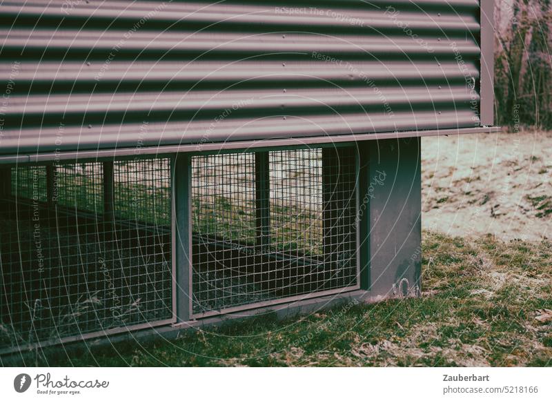 Ecke eines Zweckbaus, vergitterter Sockel, darüber Fassade aus Metall Gebäude Gitter trist öde leer grau finster reizlos Wiese Gras Bauwerk Linien Streifen