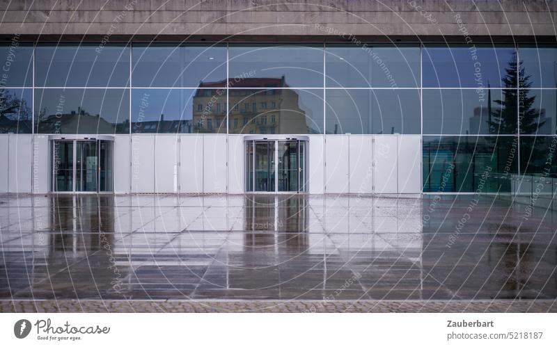 Moderne Gebäudefassade mit spiegelndem Glas und Eingangstüren, Bundespresseamt, davor großer Platz mit Steinplatten, Fassade spiegelt sich im Regen modern