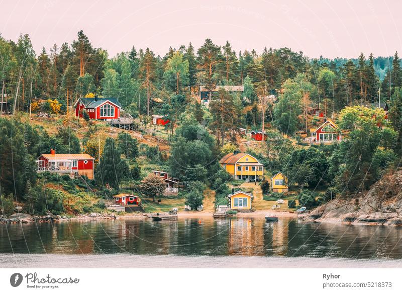 Schweden. Viele schöne rote und gelbe schwedische Holzblockhäuser Häuser auf Rocky Island Küste im Sommer Abend. See oder Fluss Landschaft Haus Hütten Hygge