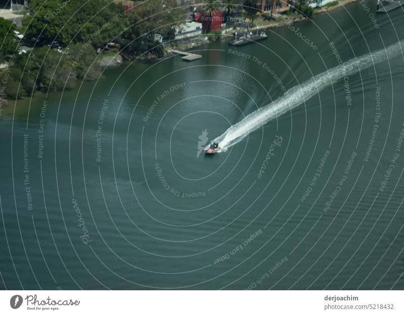 Ein Motorboot fährt mit voller Fahrt über den Fluss und einen langen Wasserschweif hinter sich zu lassen. . Motorbootsport Tag Menschenleer Farbfoto