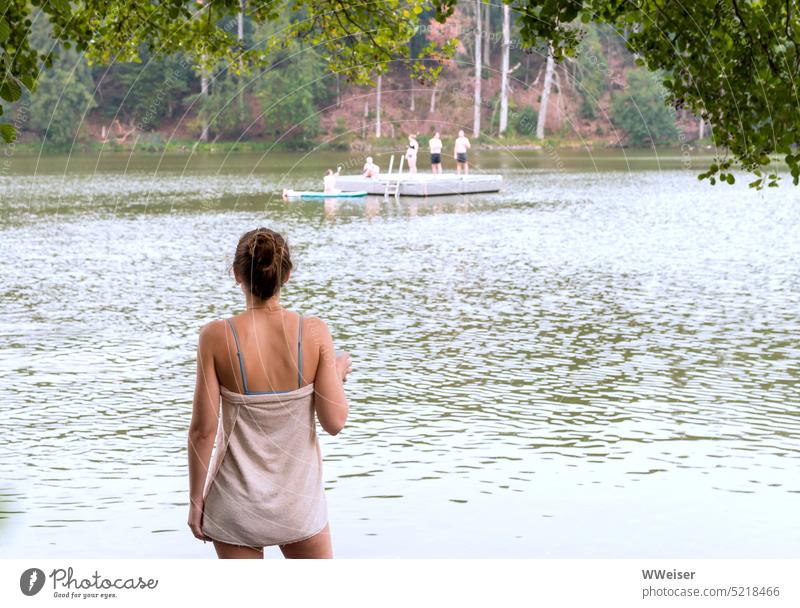 Eine junge Frau hat im See gebadet und schaut jetzt den anderen Badenden vom Ufer aus zu baden schwimmen Freizeit Wochenende Ferien Urlaub erholen zusammen