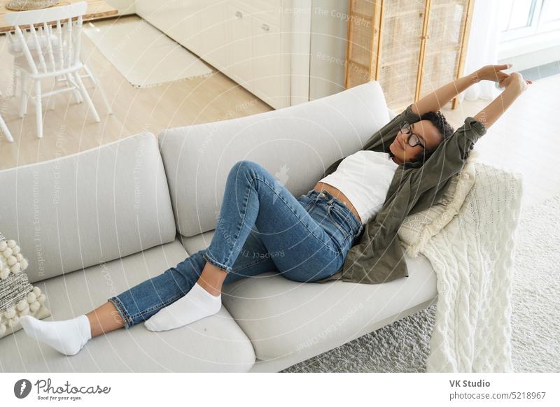 Afroamerikanisches Mädchen, das sich nach dem Mittagsschlaf streckt und auf einem bequemen Sofa im Wohnzimmer liegt Dehnung Lügen Afroamerikaner Liege