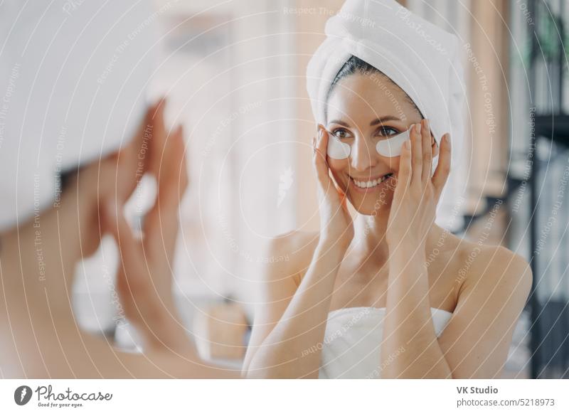 Attraktive Latina-Frau mit Augenflecken, die während der täglichen Hautpflege in den Spiegel schaut Augenbinde Bad Kosmetik Schönheit Gesundheit Gesicht
