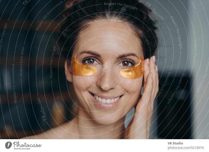Lächelnde Latina-Frau, die zu Hause feuchtigkeitsspendende goldene Pflaster unter den Augen aufträgt. Hautpflege Schönheit Routine Fleck Kosmetik Behandlung