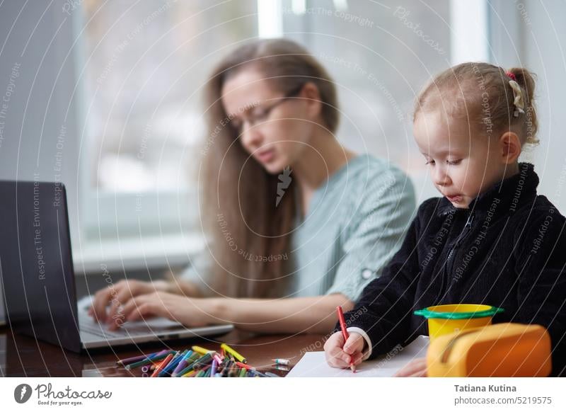 Ein Mädchen zeichnet mit Bleistiften, während es als Mutter eines Freiberuflers arbeitet. Das Konzept, zu Hause zu arbeiten und sich um die Familie zu kümmern.