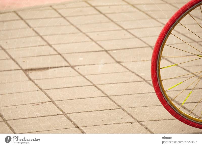 Teilansicht eines roten Fahrradreifens mit gelben Speichen auf einem gepflasterten Platz Radreifen Fahr Rad! radfahren mobil sein alternativ Straßenpflaster