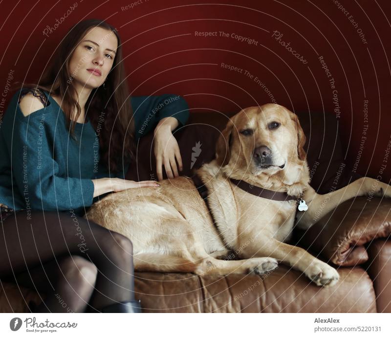 Portrait einer jungen, schönen, brünetten Frau vor einer roten Wand auf der Couch mit einem blonden Labrador - Mo, der beste Hunde der Welt Pullover türkis