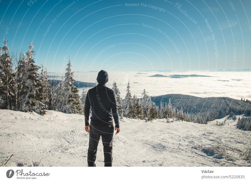 Ein begeisterter junger Reisender genießt den Blick vom höchsten Berg der Beskiden in Mitteleuropa auf die verschneite Landschaft, die bei Sonnenaufgang in der morgendlichen Inversion verschwindet