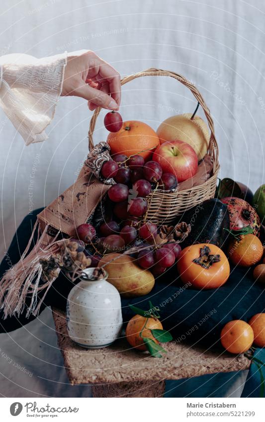 Vertikale Aufnahme einer zierlichen Hand, die eine Traube über einem Tisch hält, der mit zwölf verschiedenen runden Früchten gefüllt ist, ein philippinischer Glaube und ein Ritual, das Glück im neuen Jahr bringen soll