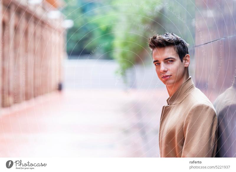 Porträt eines stilvollen, gut aussehenden jungen Mannes mit Mantel, der im Freien steht und sich an eine Wand lehnt. Erwachsener Fotokamera Kaukasier