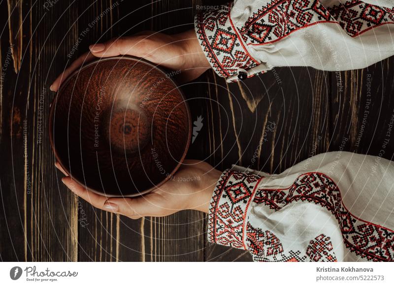Weibliche Hände mit leerer ukrainischer Tonschale auf Holztisch. Platz zum Kopieren. Antiquität Schalen & Schüsseln braun Keramik Tonplatte Tonkeramik Farbe