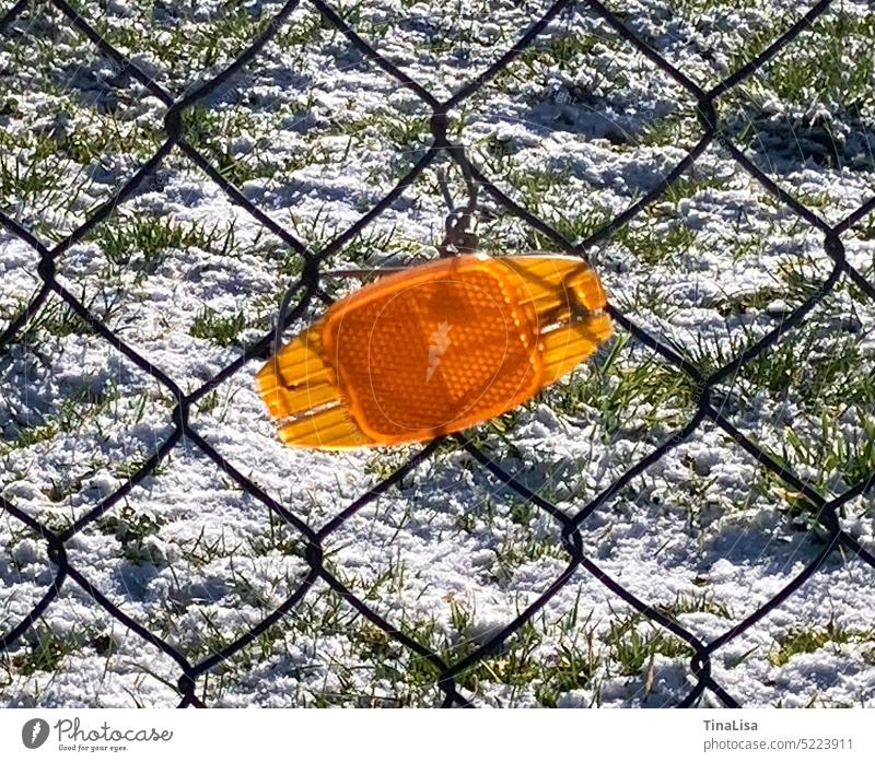 Reflektor Katzenauge am Zaun orange Außenaufnahme Detailaufnahme Farbfoto Schnee Gras