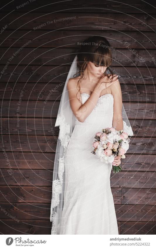 schöne junge Braut in einem luxuriösen weißen Kleid mit einem Blumenstrauß in der Hand auf einem hölzernen Hintergrund im Freien hochzeitlich Stil Mädchen