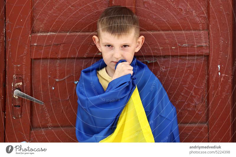 Ukrainisches Kleinkind steht im Freien und unterstützt sein Heimatland, kleines Kind mit Nationalflagge schaut in die Kamera. Protest gegen den russischen Krieg in der Ukraine, bewaffneter Konflikt, obdachlos, Krise, Porträt