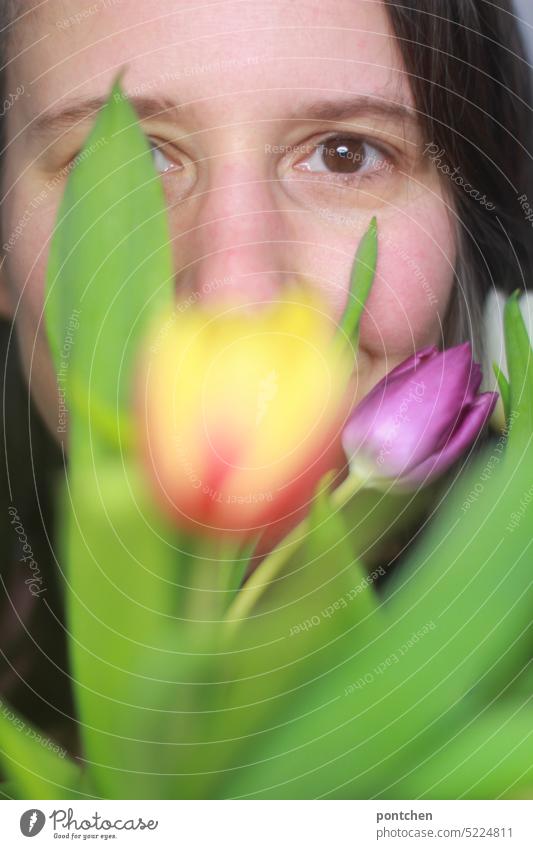 etwas durch die blume sagen. gesicht einer lächelnden frau, verdeckt durch einen strauß tulpen blumenstrauß frühlingsgruß versteckt portrait auge brünett schön