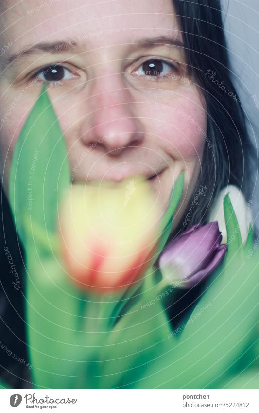 lächelnde frau vor einem tulpenstrauß, der ihr gesicht teilweise verdeckt fröhlich frühling blumenstrauß geschenk Blume Blüte schön Tulpe muttertag valentinstag