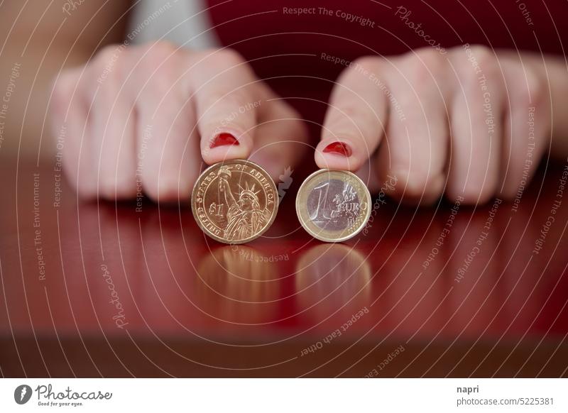 1:1 | 1 Dollar und 1 Euro Münze von Zeigefingern mit rot lackierten Fingernägeln auf einer Tischplatte gehalten. Geld Geldmünzen dollar € $ Bargeld Münzen