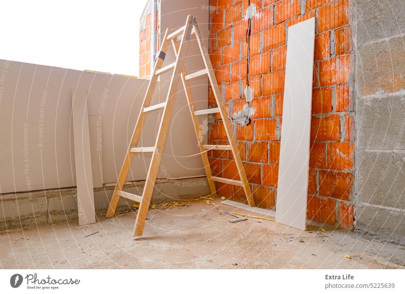 Holzleiter auf der Baustelle, Gipskartonplatte lehnt an einer Wand aus Blöcken in einem unfertigen Gebäude Appartement Klotz Holzplatte Baustein Kabel Zement