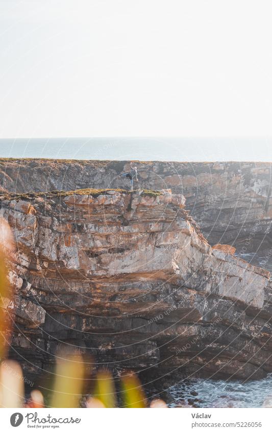 Wanderer feiert seinen Erfolg. Atemberaubende Klippen mit Kieselstrand in der Nachmittagssonne an der Atlantikküste bei Vila Nova de Milfontes, Odemira, Portugal. Auf den Spuren der Rota Vicentina