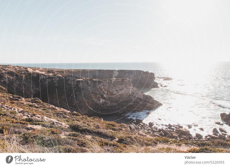 Atemberaubende Klippen mit einem Kieselstrand in der Nachmittagssonne an der Atlantikküste bei Vila Nova de Milfontes, Odemira, Portugal. Auf den Spuren der Rota Vicentina. Fischerpfad