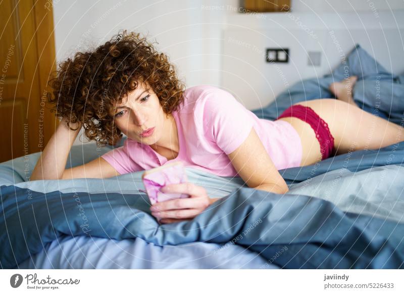 Charmante Frau mit Textnachrichten auf dem Smartphone im Bett benutzend schmollende Lippen Komfort soziale Netzwerke Süchtige Morgen heimwärts Schlafzimmer