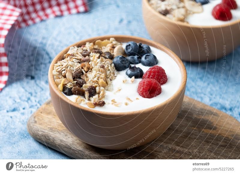 Joghurt mit Beeren und Müsli zum Frühstück in Schale auf blauem Hintergrund Blaubeeren Himbeeren Frucht Muttern Zerealien Griechen Molkerei Rosinen Gesundheit
