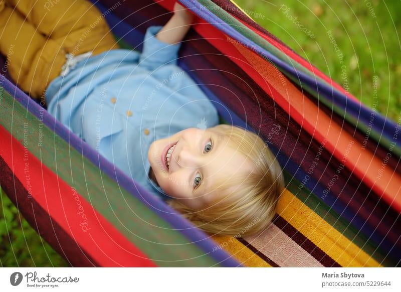 Nette kleine blonde weiße Junge genießen und Spaß haben mit bunten Hängematte im Hinterhof oder Spielplatz im Freien. Sommer im Freien aktive Freizeit für Kinder. Kind