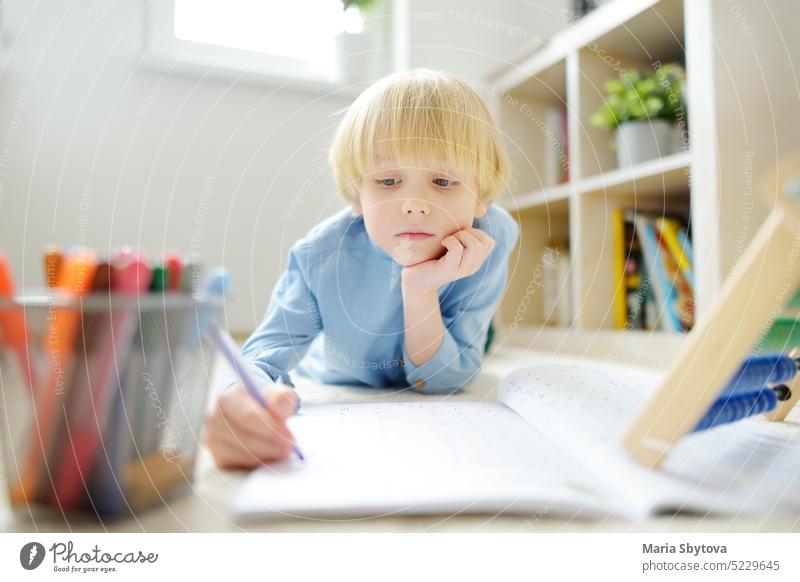 Grundschüler Junge macht Hausaufgaben auf dem Boden zu Hause. Kind lernt zu zählen, löst arithmetische Beispiele im Arbeitsbuch. Mathe-Übung. Preparing Vorschüler Baby für die Schule.