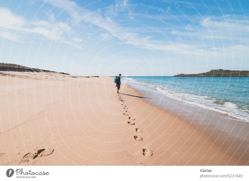 Leidenschaftlicher Rucksacktourist, Rucksack und Stiefel in der Hand, spaziert am Strand Praia da Ilha do Pessegueiro am Atlantik in der Nähe von Porto Covo, Portugal. Auf den Spuren der Rota Vicentina