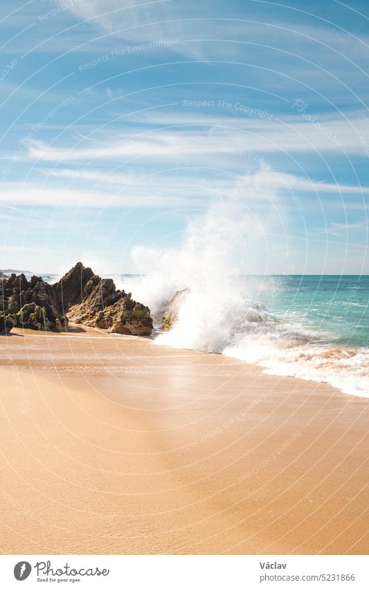 Die Wellen des Atlantiks schlagen an einem sonnigen Tag gegen einen Felsen am Sandstrand von Praia da Ilha do Pessegueiro in der Nähe von Porto Covo, Westportugal. Rota Vicentina