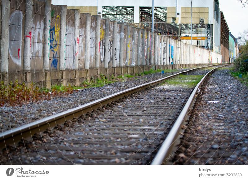 Eisenbahnschienen entlang einer Betonmauer im Industriegebiet Gleise Schienen Schienenverkehr Graffiti Industriehalle Transportweg