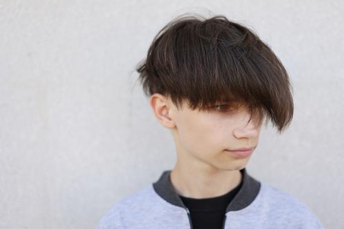Schöner junger Mann mit stilvollem Haarschnitt. Porträt von Teenager-Junge mit Jugendfrisur steht auf grauem Hintergrund. Gesicht gutaussehend Lifestyle Frisur