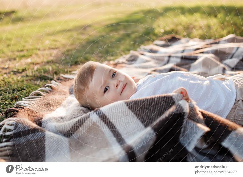 Glücklich adorable Baby Junge liegt auf der Decke auf dem Gras im Park am Sommertag. Kind in trendy und niedliche Kleidung Wiese Löwenzahn schön Spaß wenig