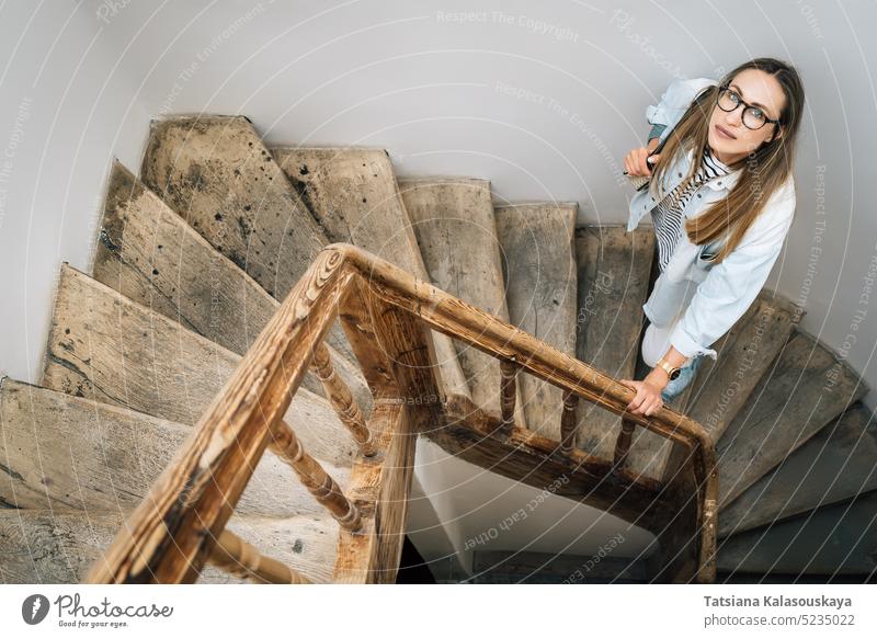 Eine Frau schaut auf einer alten Holztreppe stehend nach oben nachschlagen aufschauend Stehen hölzern Treppenhaus Menschen Person Erwachsener langhaarig allein