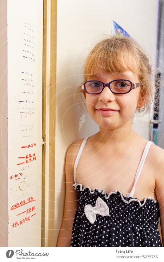 Porträt eines süßen kleinen Mädchens mit Brille und ihren Größenmaßen an der Tür 7 bezaubernd schön Pflege Kaukasier Kind Kindheit Termin & Datum Dipodisch