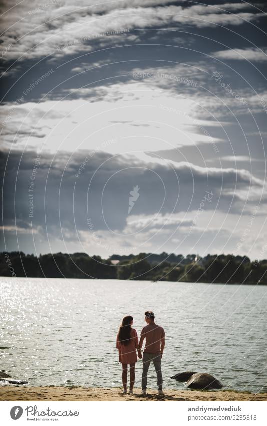 schöne Paar steht am Wasser entlang Flussufer, halten die Hände zusammen, glückliche Familie Konzept. Liebesgeschichte See Mann Sommer Zusammensein Frau jung