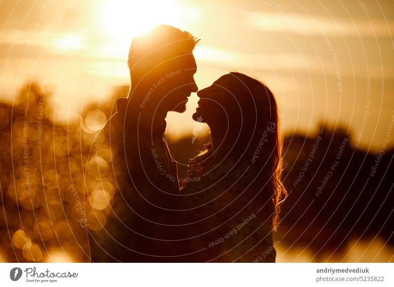 Silhouette eines liebenden Paares, das sich bei Sonnenuntergang auf dem See umarmt. Schönes verliebtes junges Paar, das bei Sonnenuntergang in den Strahlen des hellen Lichts am Ufer des Sees spazieren geht. copy space. selective focus
