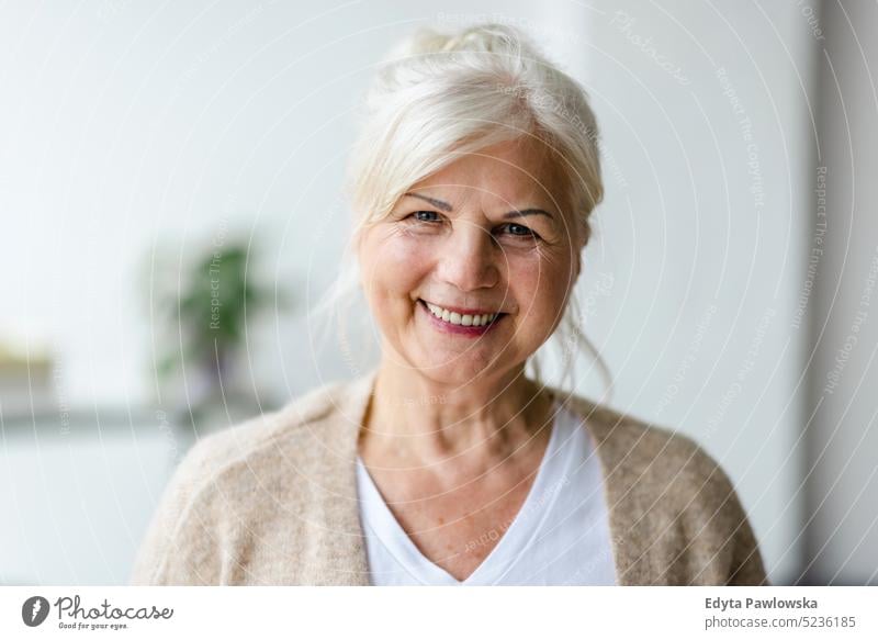 Porträt einer lächelnden älteren Frau, die in die Kamera schaut echte Menschen Senior im Innenbereich Loft Fenster heimwärts reifer Erwachsener eine Person