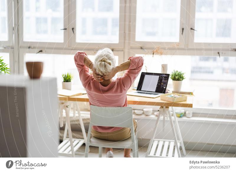 Entspannte ältere Frau, die am Tisch im Büro sitzt echte Menschen Senior im Innenbereich Loft Fenster heimwärts reifer Erwachsener eine Person attraktiv