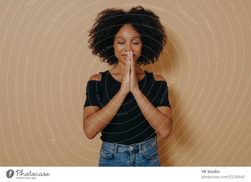 Afroamerikanische junge Frau, die betet und die Hände zum Gebet hält, stehend im Studio Afroamerikaner Afrikanisch betend Beteiligung gestikulieren Atelier