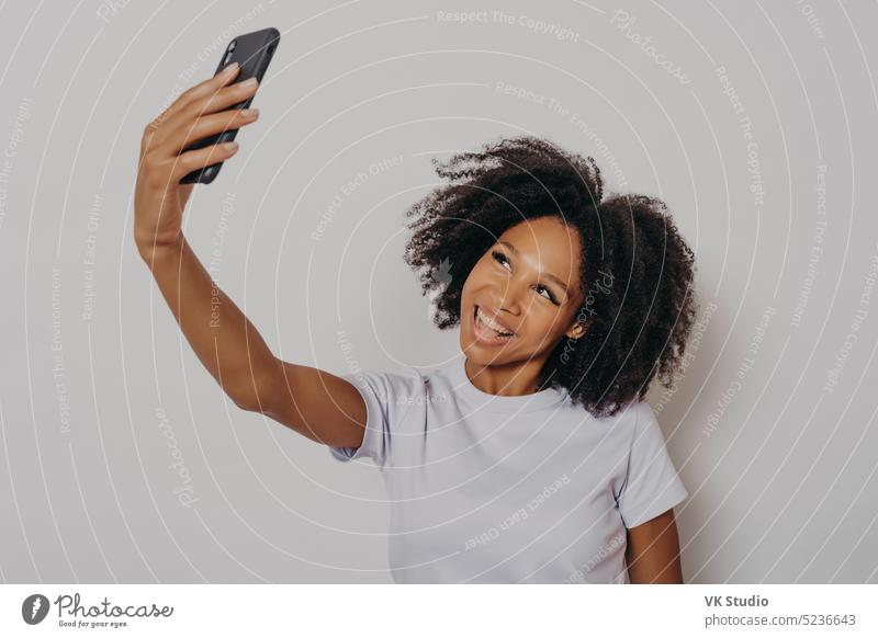Fröhliche junge afrikanische Frau mit lockigem Haar, die ein Selfie mit ihrem modernen Mobiltelefon macht Afro-Look Amerikaner Foto Hintergrund Smartphone