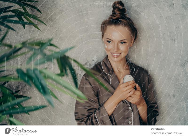 Junge kaukasische attraktive Frau in Seide braunen Pyjama tun Hautpflege Verfahren zu Hause Schönheit jung Lächeln anwendend Gesicht Sahne Kosmetik Routine