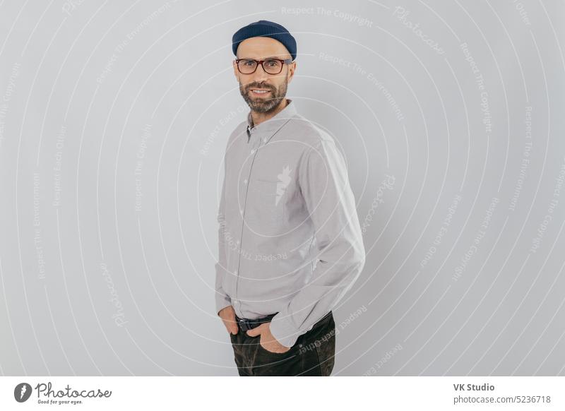 Profilaufnahme eines attraktiven, unrasierten Mannes, formell gekleidet, trägt eine optische Brille, modelliert vor weißem Hintergrund, freut sich über gute Ergebnisse bei der Arbeit, hat einen zufriedenen Gesichtsausdruck. Menschen und Stil