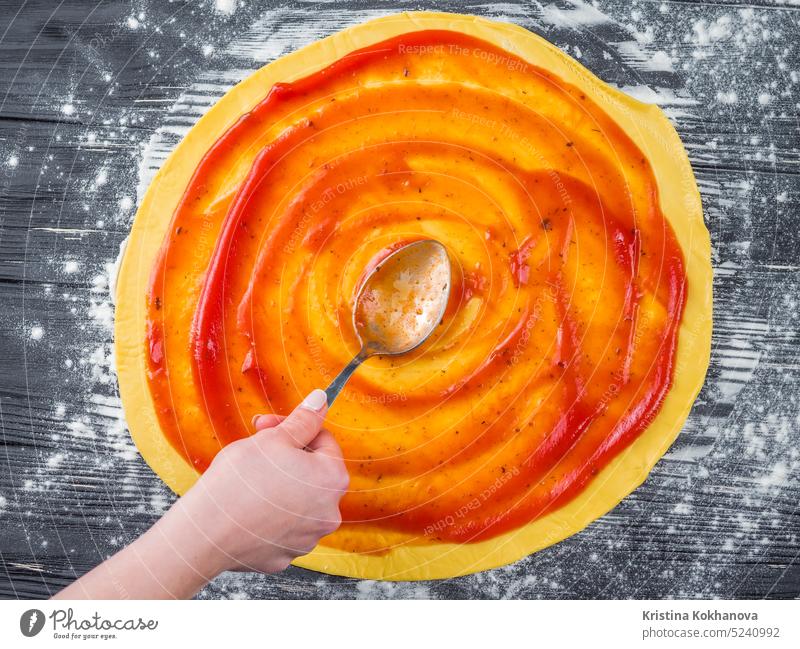 Weibliche Hand fügt rote Soße hinzu. Italienische Pizza Zubereitung auf blauem Holztisch. Kochen Konzept. Saucen Herstellung Prozess Küchenchef backen blanko