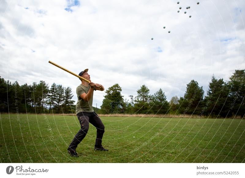 Junger Mann versucht heranfliegende Golfbälle weg zu schlagen Bälle Action abwehren Bälle schlagen viele Spielwiese Überforderung verteidigen zu viele Abwehr